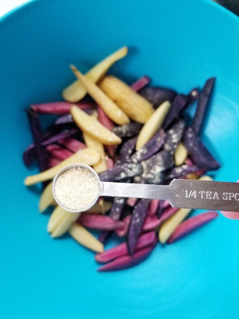 adding spice to rainbow potato fries in a mixing bowl