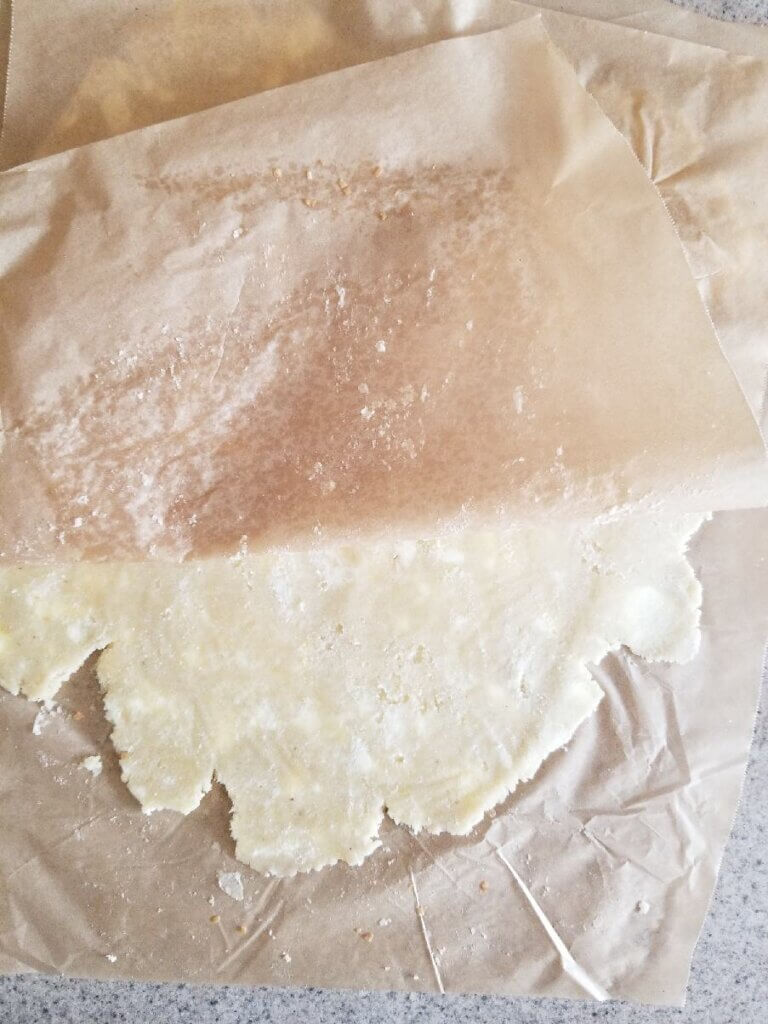 almond flour pie crust rolled flat between 2 pieces of parchment paper