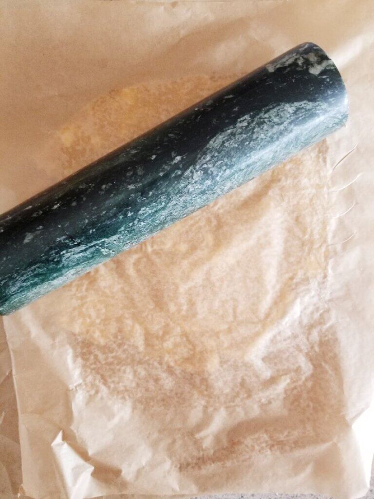 rolling almond flour pie crust between 2 pieces of parchment paper