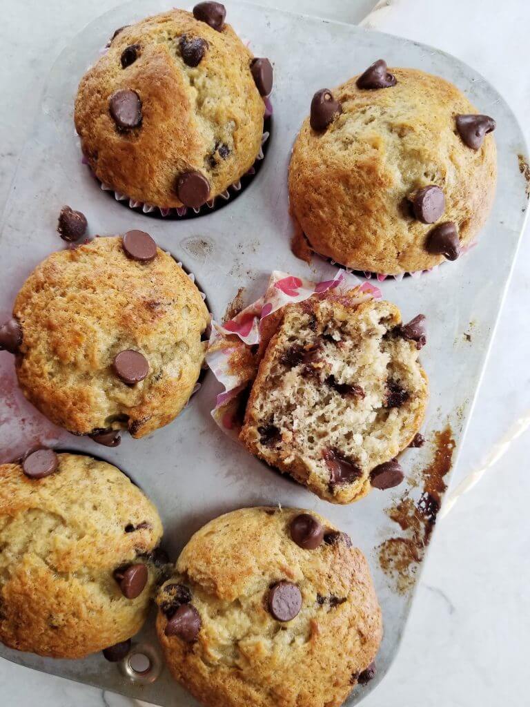 sourdough banana chocolate chip muffins in a muffin tin showing one cut in half for its texture