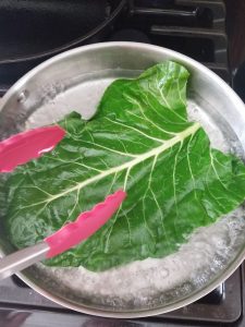 blanching a collard green in a pan of boiling water using red tongs