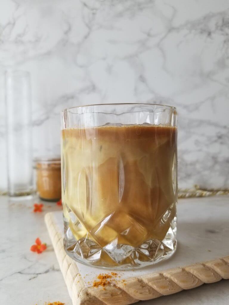 iced golden milk latte in a crystal glass with golden milk latte mix in the background