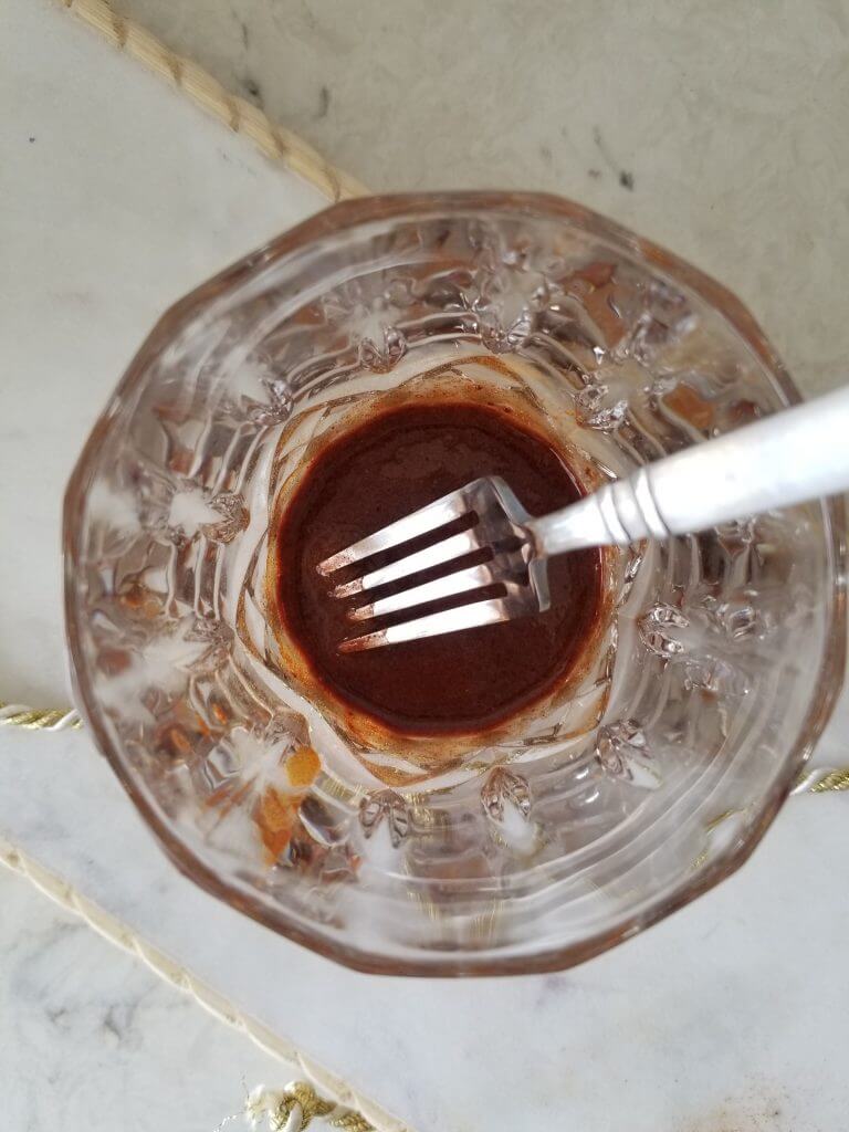 golden milk latte in a glass mixed into maple syrup using a fork