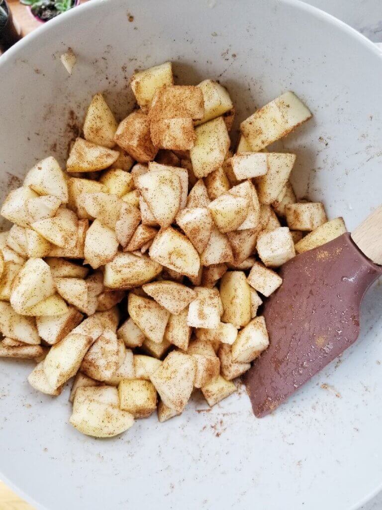 apple chunks tossed with cinnamon in a mixing bowl
