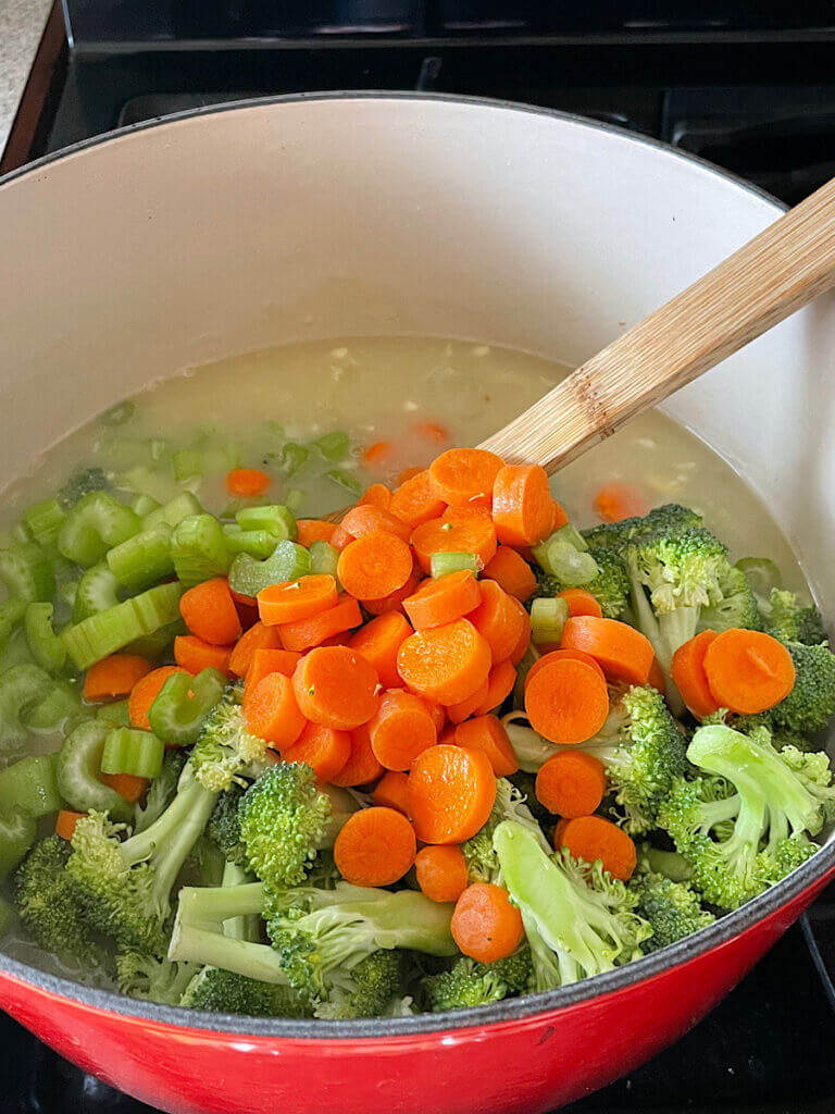 adding carrots broccoli and celery to a pot