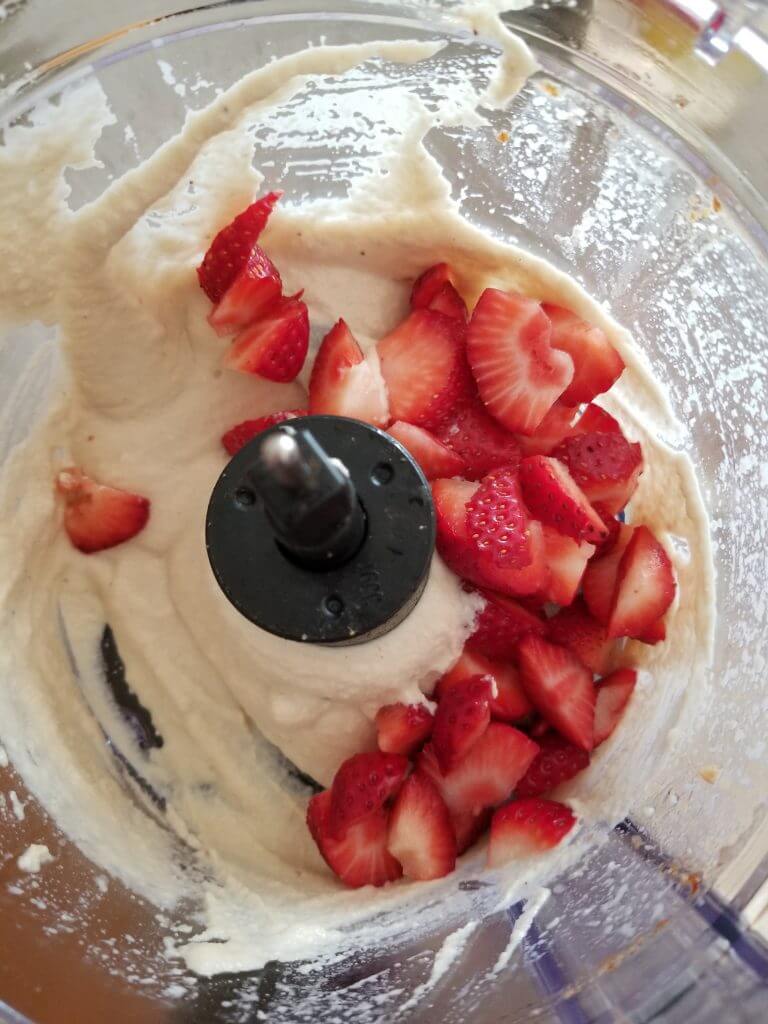 adding strawberries to the cashew filling in the food processor