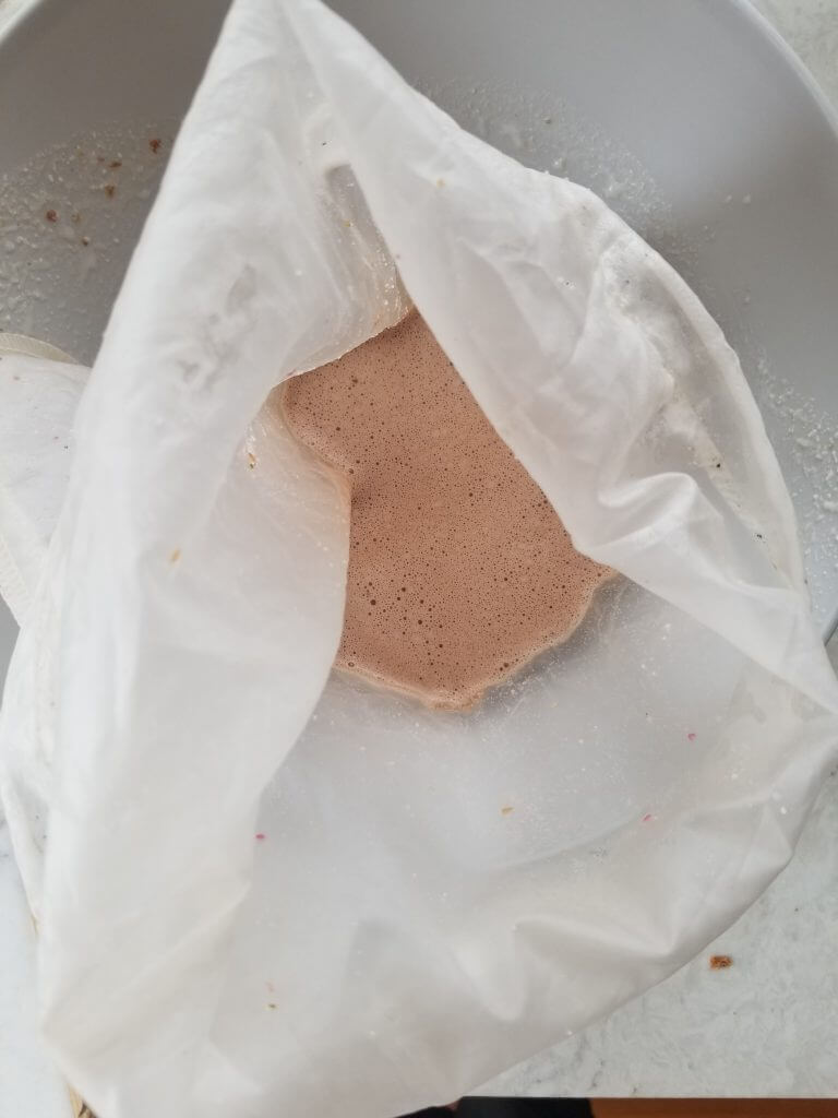 straining chocolate almond milk through a nut milk bag