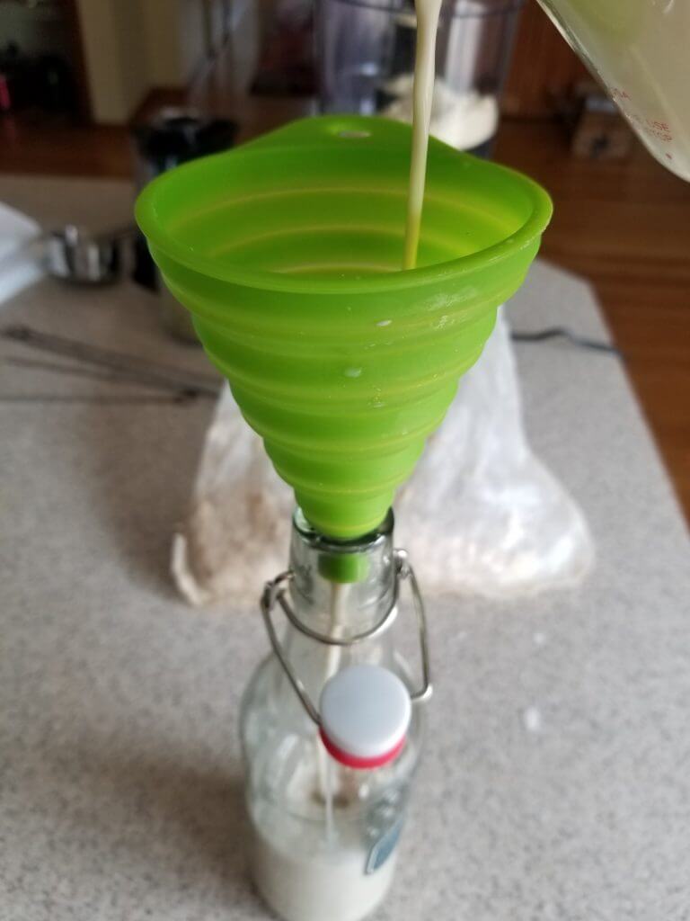 using a funnel to fill a glass jar with the fresh made Vanilla almond milk creamer