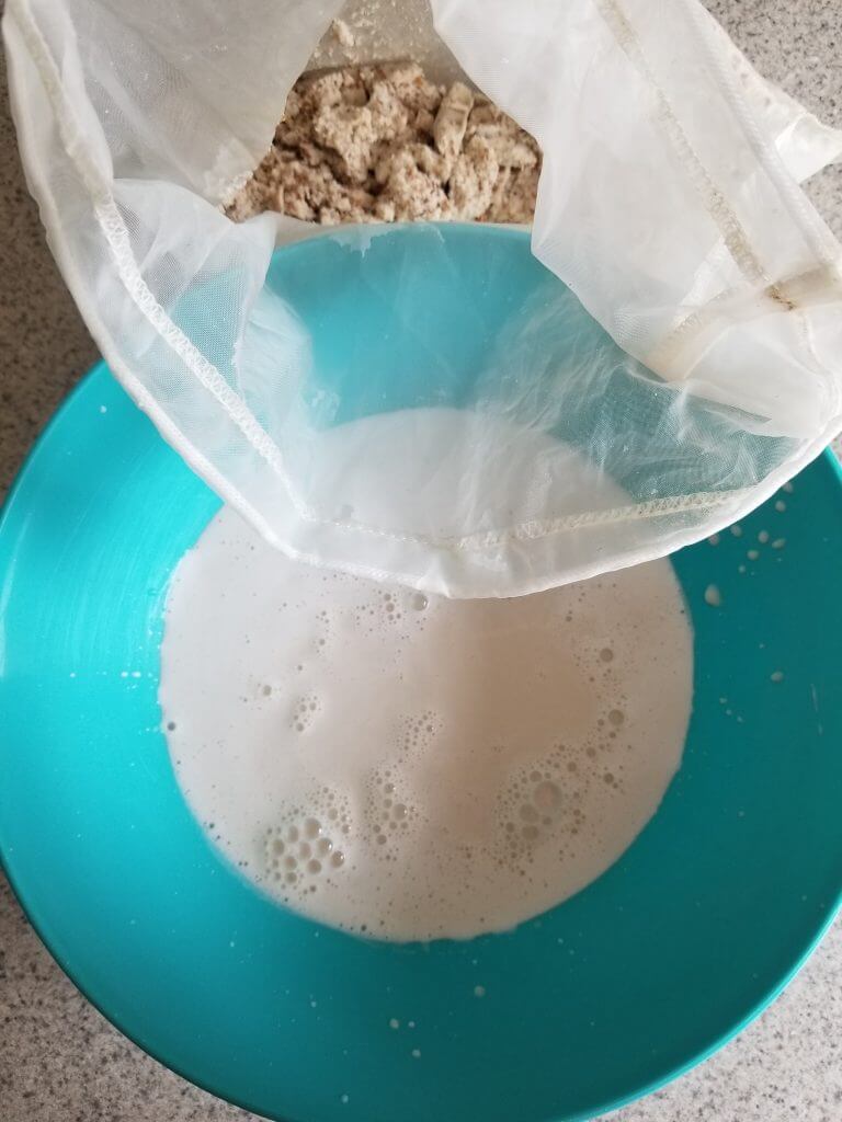 Vanilla almond milk creamer in a blue bowl with the almond pulp on the side in a nut milk bag