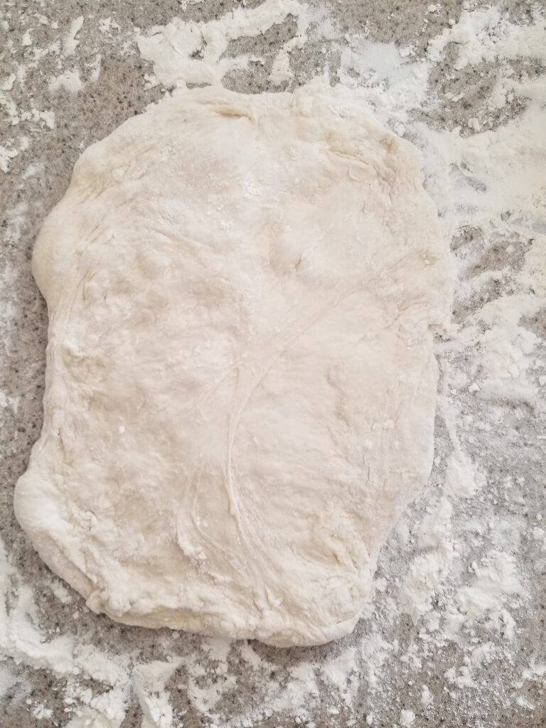 homemade ciabatta bread pressed into a rectangle on the floured counter top