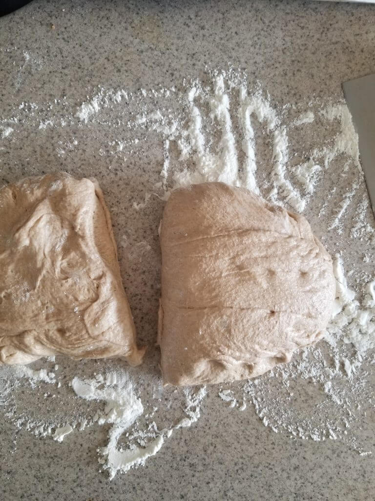 dividing whole wheat ciabatta bread dough in half to form 2 loaves on a floured surface