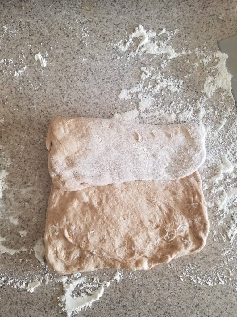 folding whole wheat ciabatta bread on a floured surface