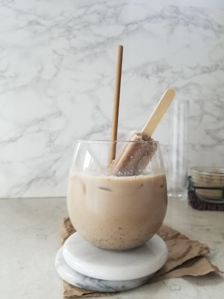 stemless wine glass with matcha maca cacao powder mixed into milk with a coffee Popsicle sticking out the top