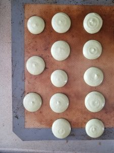 piped matcha macarons on baking mat to dry before baking