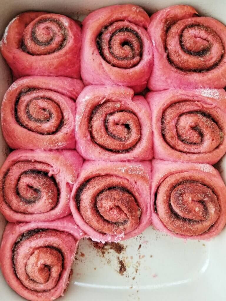 pink cinnamon rolls in a red pan after baking
