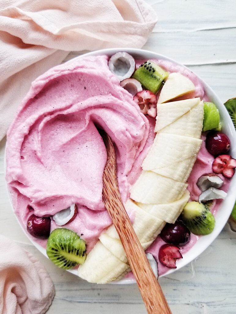 pink smoothie bowl topped with banana, kiwi, and fruit
