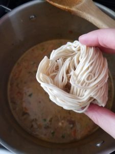 Adding the final ingredient to the large pan of ramen noodle soup