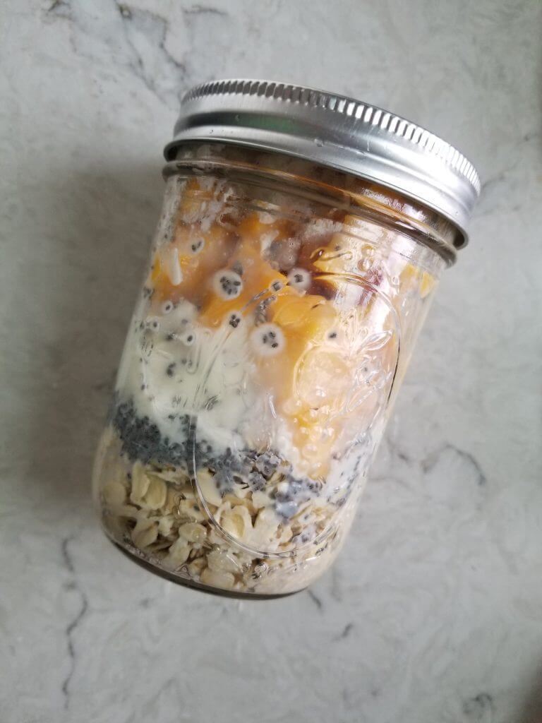 mason jar with layered oats, chia seeds, yogurt, milk, and mangoes