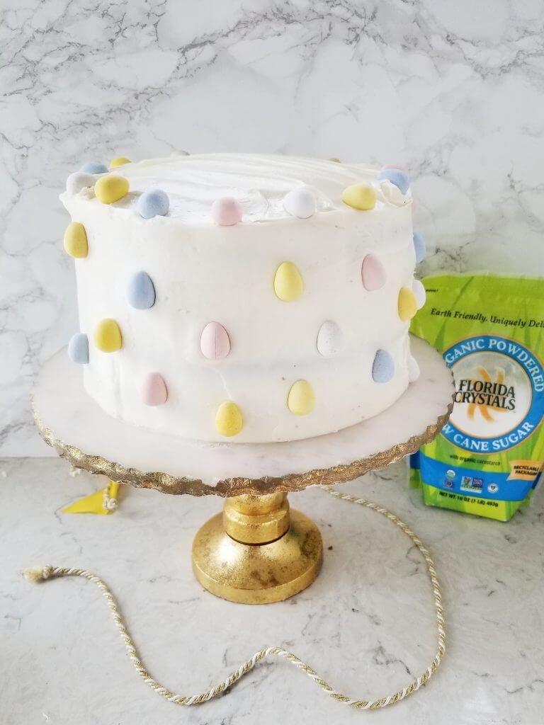 surprise carrot cake before it is cut open sitting on a gold and marble cake stand with yellow, pink, and blue chocolate covered eggs